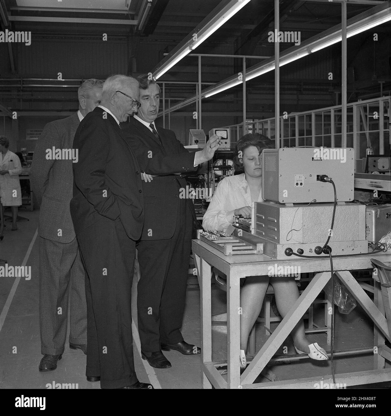 1960s, historique, sur le site de production d'une usine de radio, a adapté  les cadres de l'entreprise debout à côté d'une femme technicien assis à son  poste de travail, discutant des questions