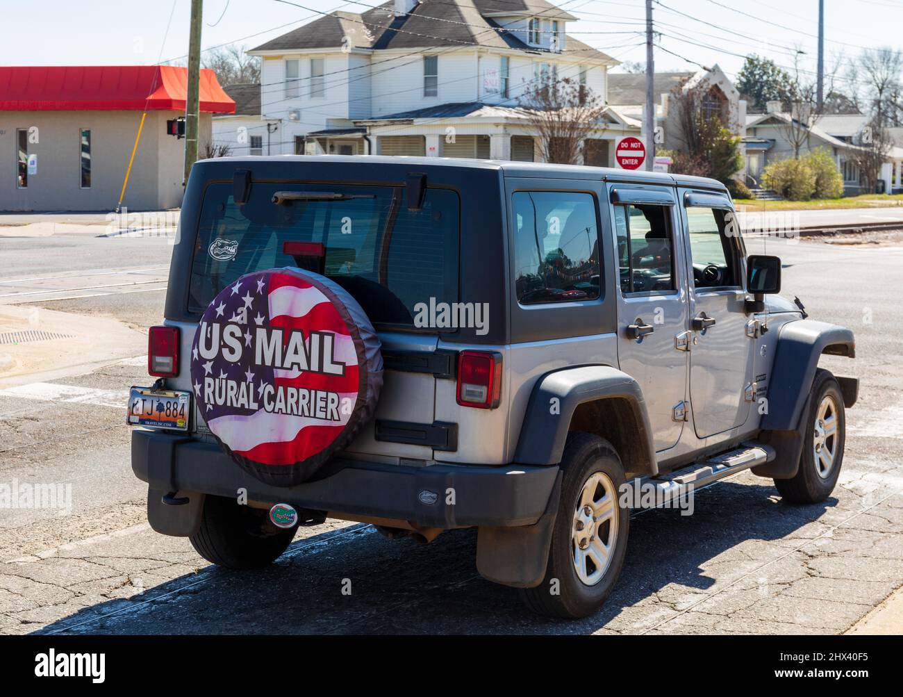 GASTONIA, NC, USA-3 MARS 2022: Jeep Wrangler de modèle récent avec couvercle de pneu arrière indiquant 'US Mail Rural Carrier' sur fond de drapeau américain. Banque D'Images