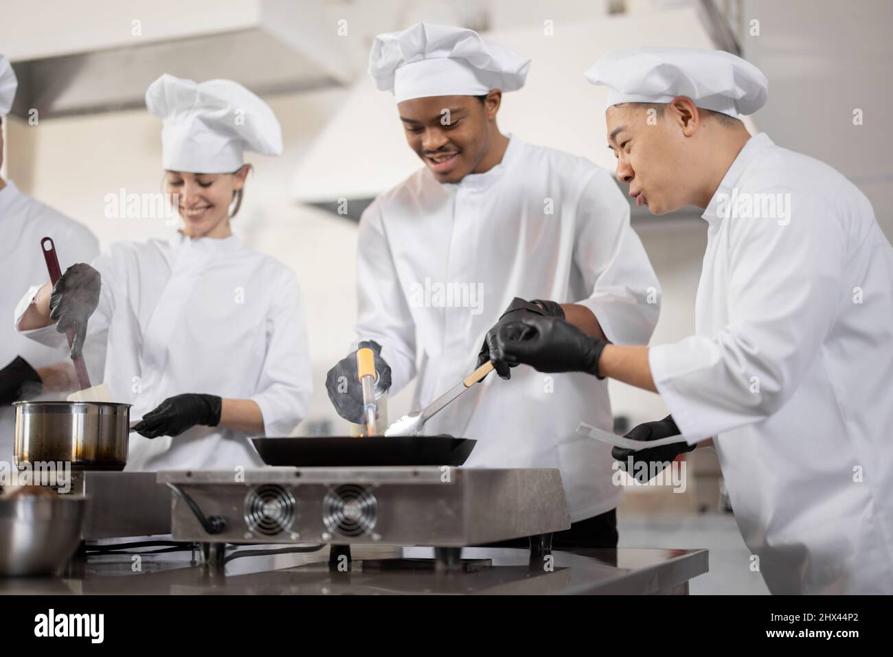 Équipe multiraciale de cuisiniers professionnels en uniforme préparant des  repas pour un restaurant dans la cuisine. Chef asiatique gérant le  processus, le type latin et les cuisiniers européens friture. Travail d' équipe et