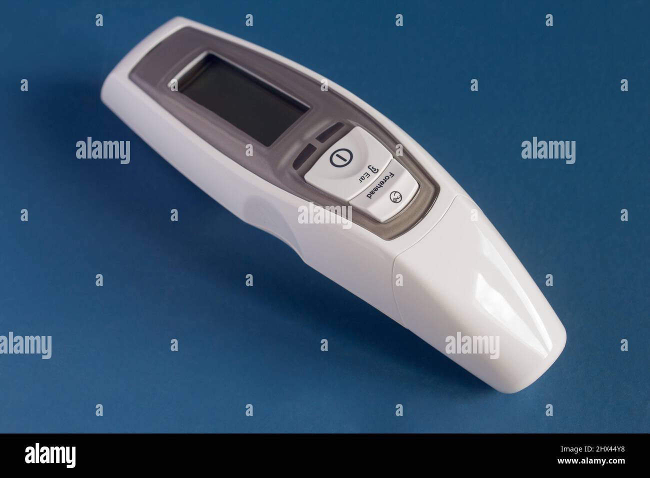 Thermomètre laser frontal et auriculaire avec écran LCD et alarme de fièvre sur fond bleu studio. Médecine et technologie. Banque D'Images