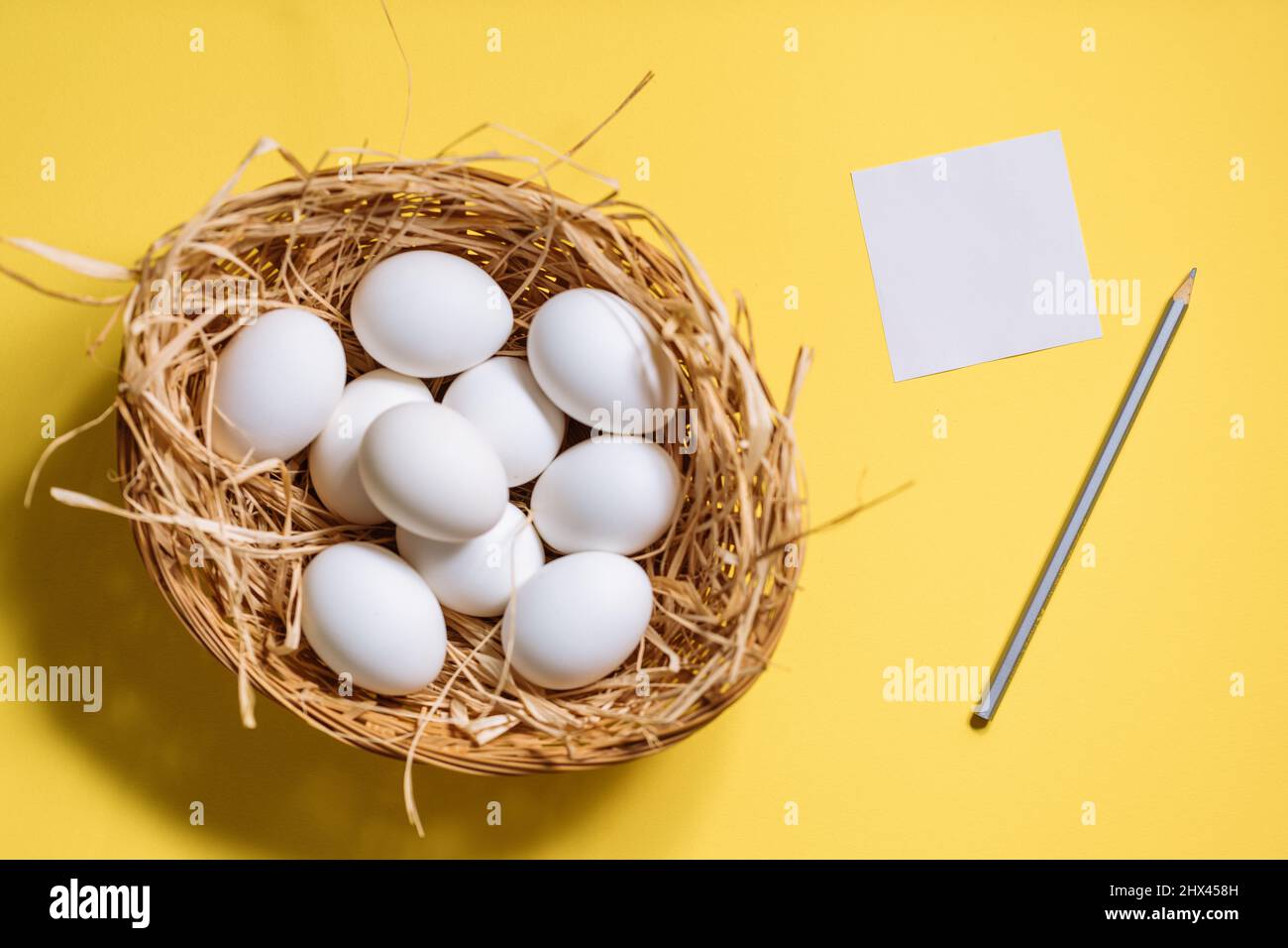 Œufs de pâques blancs dans un panier jaune avec paille sur fond jaune. Vue de dessus du concept de carte postale joyeuses Pâques Banque D'Images