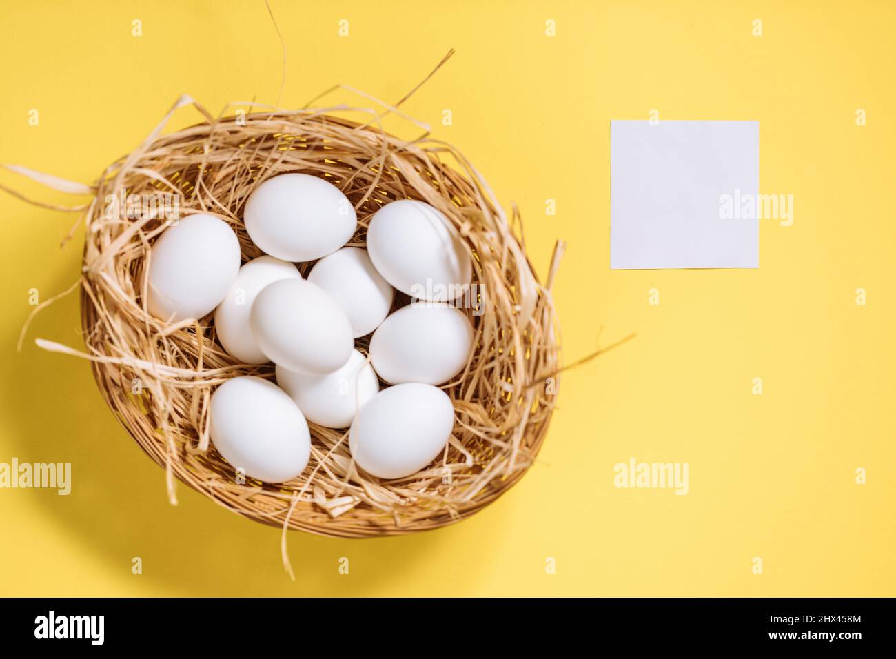 Œufs de pâques blancs dans un panier jaune avec paille sur fond jaune. Vue de dessus du concept de carte postale joyeuses Pâques Banque D'Images