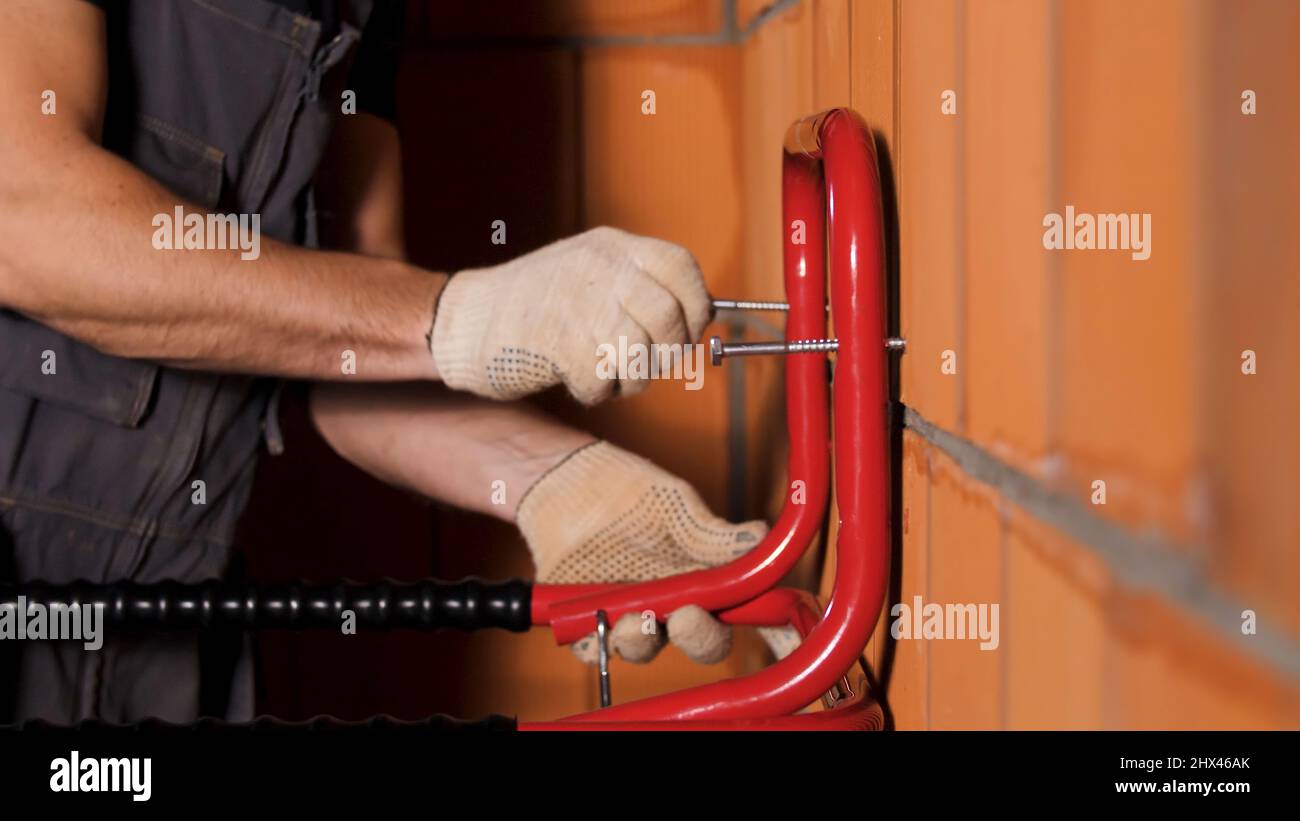 Vue latérale d'un travailleur qui pendait un objet métallique lourd sur le mur en blocs de céramique. Gros plan des mains mâles dans des gants de protection en serrant la vis Banque D'Images