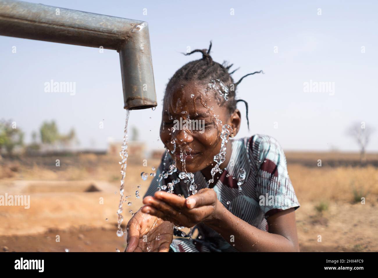 Gros plan d'une belle fille africaine se lavant le visage au point d'eau de la communauté publique ; problème social de pénurie d'eau et de distribution inadéquate Banque D'Images