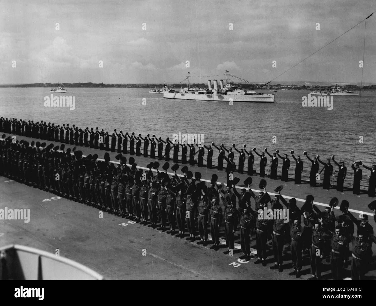 Les Aussiens applaudissent la Reine à Spithead - des hommes de l'armée australienne qui ont pris part à la procession du couronnement le 2 juin donnent trois encouragements du pont de vol du porte-avions australien HMAS Sydney (14 000 tonnes, déplacement standard, 17 700 pleine charge) Alors que le Royal Yacht 'Surprise' (non illustré) passe lors du coroner Naval Review de 300 navires de guerre à Spithead, en Angleterre, aujourd'hui 15 juin. En arrière-plan est le Cruiser Devonshire (9 850 tonnes). 15 juin 1963. (Photo par photo de presse associée). Banque D'Images