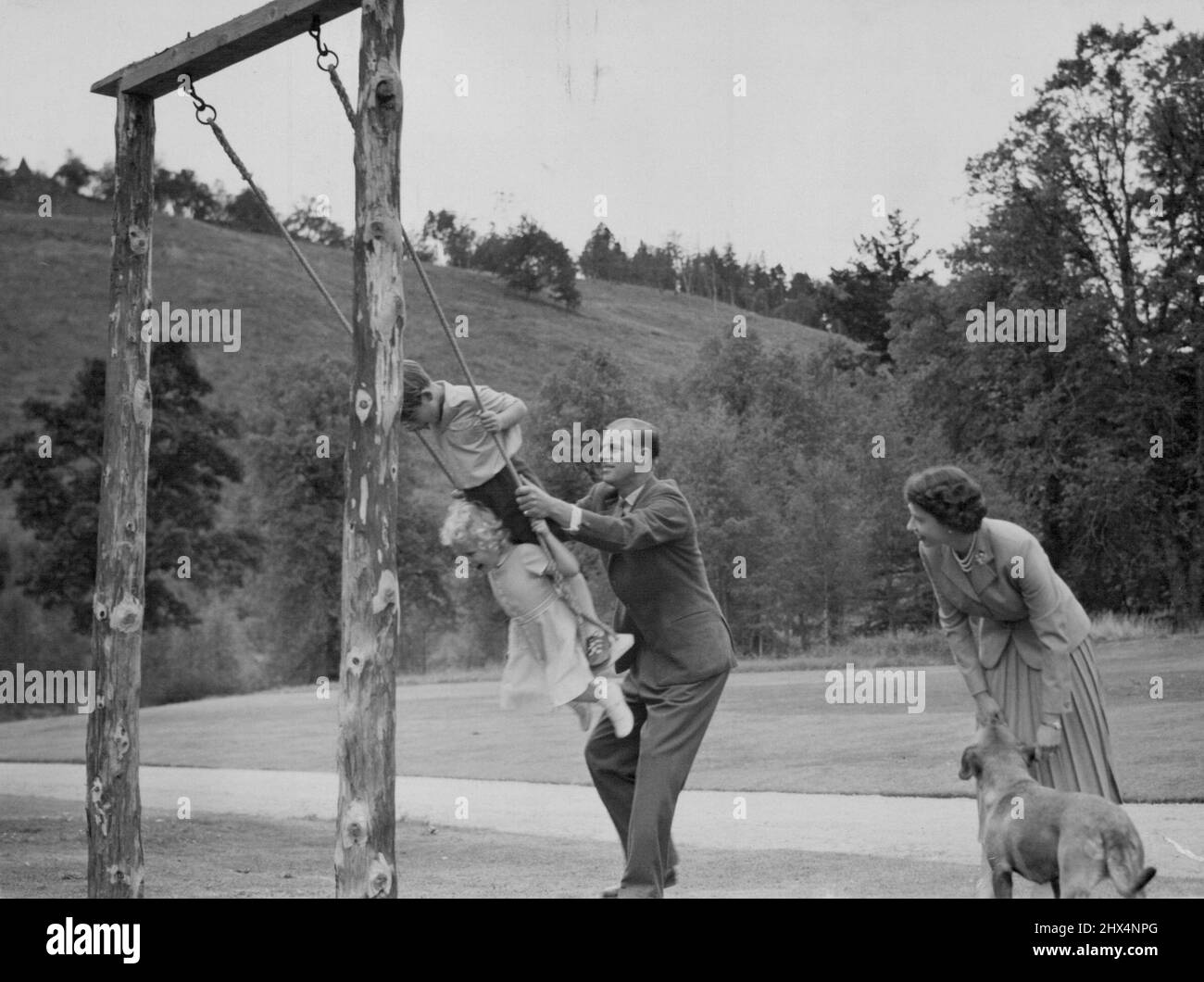 La famille royale à Balmoral le duc d'Édimbourg fournit le « Push » pour le prince Charles et la princesse Anne lorsqu'ils jouent sur une aile dans le parc du château de Balmoral pendant les vacances d'été de la famille royale en août 1955. La Reine regarde, avec le chien corgi du duc 'Candy'. Le château Balmoral, propriété privée du souverain, était la résidence préférée de la reine Victoria. Il est sur décision, West Aberdeenshire, Écosse. 26 septembre 1955. (Photo de James Reid, Associated Press photo). Banque D'Images