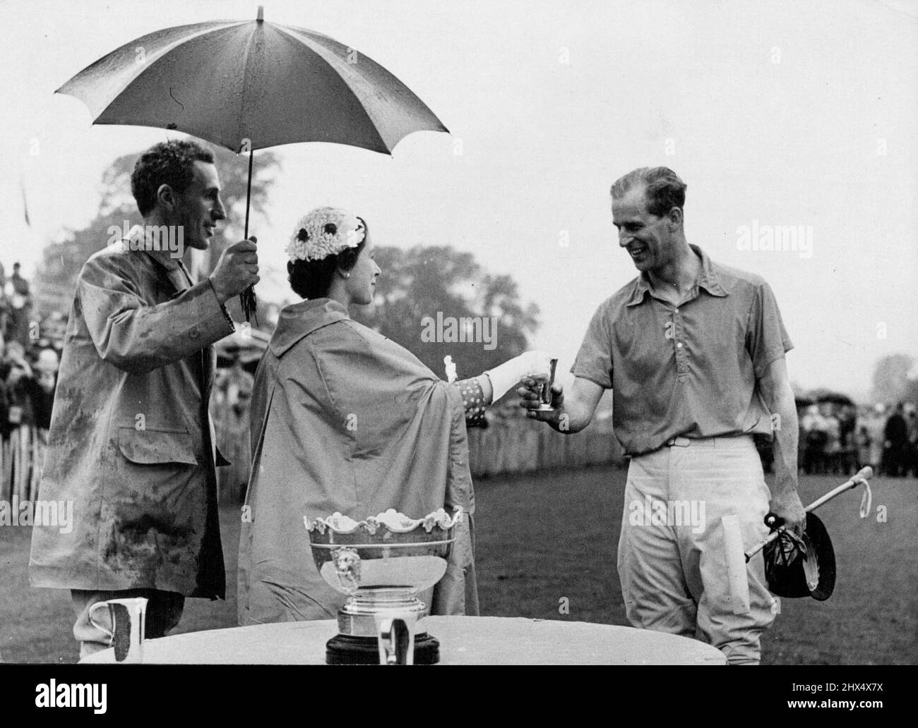 Une coupe pour le duc - de la Reine -- au parc de compagnie, Sussex, hier, l'équipe de polo du duc a battu Whiphill 5 - 0 dans la finale des novices. Il y avait une tasse à présenter au capitaine de l'équipe gagnante, et la Reine était là pour la présenter. C'est donc que la Reine, protégée de la pluie par un parapluie, a présenté la coupe à son mari. 22 juin 1953. (Photo de Paul Popper, Paul Popper Ltd.). Banque D'Images