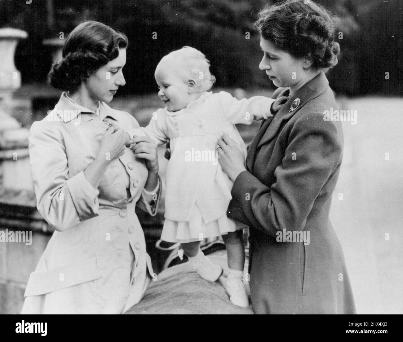 La famille royale à Balmoral : Une charmante étude des sœurs royales prises lors d'un de ces heureux rassemblements familiaux. Il montre la princesse Elizabeth (à droite) et la princesse Margaret aider à équilibrer le bébé princesse Anne sur une balustrade dans le parc du château. Comme tous les bébés, la princesse Anne aime les objets pétillants et joue de grand cœur avec la broche de la princesse Margaret. Le roi, la reine et la princesse Margaret, qui résident au château de Balmoral, en Écosse, reçoivent de fréquentes visites de la princesse Elizabeth et du duc d'Édimbourg, séjournant à Birkhall tout proche. L'approbation royale a été donnée pour le publ Banque D'Images