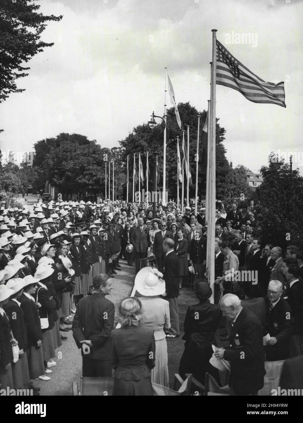 Drapeau américain est levé à Uxbridge : comme le drapeau américain est sécurisé par un préposé de kilted, après avoir été levé par Mme Lewis Douglas, épouse de l'ambassadeur américain (troisième femme de gauche, de retour à la caméra, en premier plan), Boery Brundage (debout, au centre) président de l'American Athletic Association, S'adresse aux membres de l'équipe olympique américaine au camp d'Uxbridge (Middlesex) ce matin, le 22 juillet. L'homme debout à l'extrême gauche (premier plan, retour à la caméra) est le très honorable Lord Burghley, président du comité d'organisation des Jeux Olympiques. Derrière lui, un peu à droite, est Mlle Banque D'Images