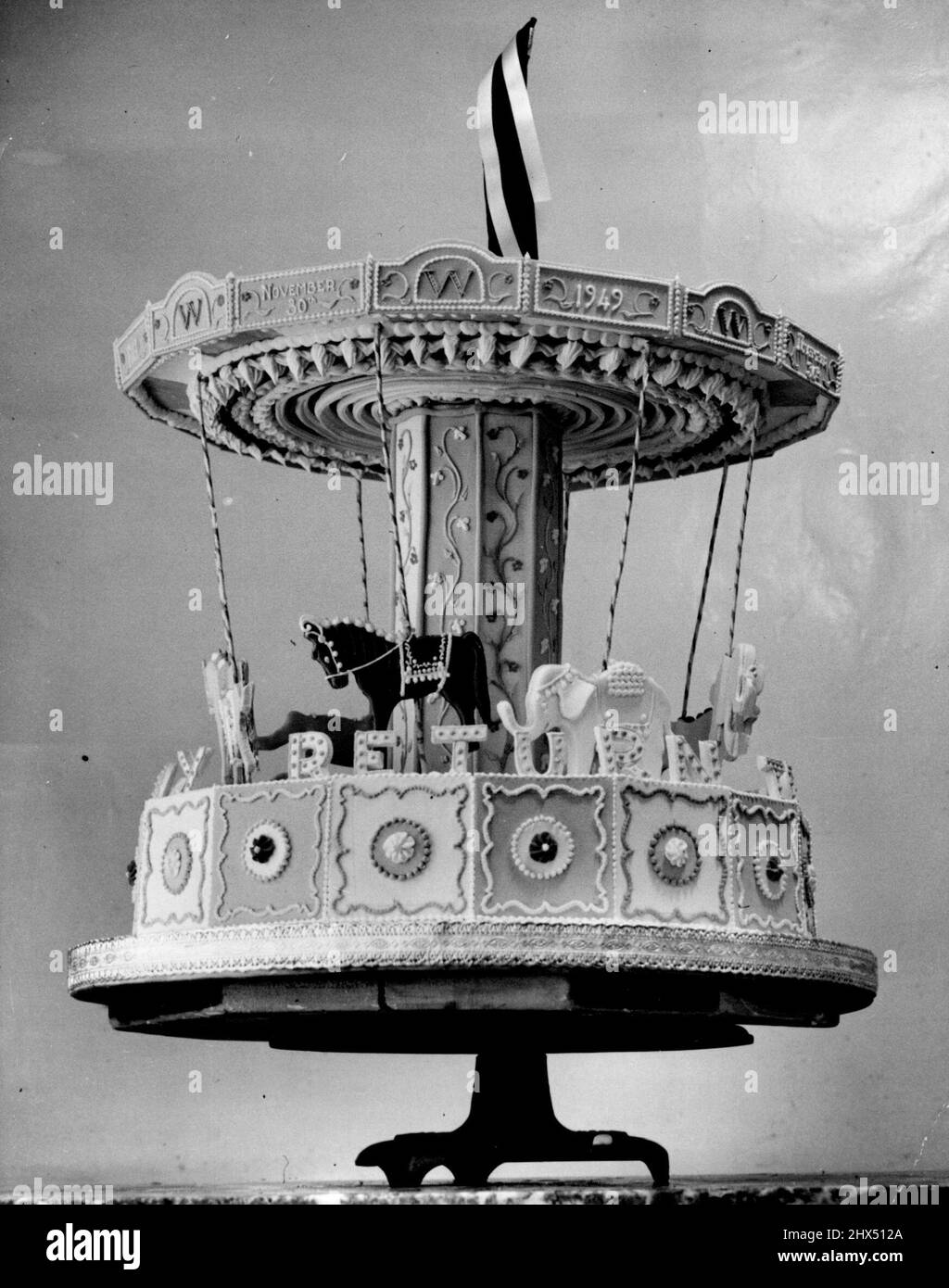 Gâteau d'anniversaire 75th « Merry-Go-Round » de Winston -- lieu d'honneur sur la table à morrow de M. Winston Churchill (mercredi) va à ce gâteau ingénieux et finement modélisé, spécialement fait par Mme. Floris de Londres pour son anniversaire de 75th.le gâteau Merry-Go-Round, richement décoré et décoré avec des chevaux et des éléphants camarisonés gaious, porte l'inscription inhabituelle : « Pour vous souhaiter un retour heureux ».seules les parties non comestibles du gâteau sont les couleurs de course de M. Churchill, flottant de façon géante au-dessus du joyeux-tour.l'entreprise, les fabricants des gâteaux d'anniversaire de la famille Churchill pendant de nombreuses années, ont également été responsables Banque D'Images