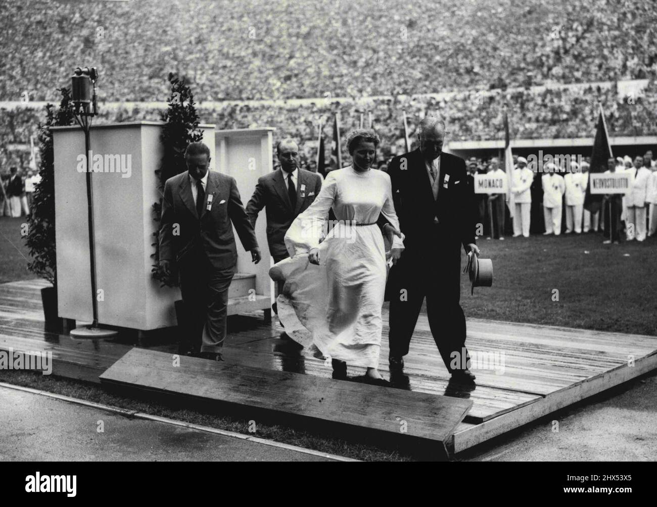 Woman in White donne un sensationnel début aux Jeux Olympiques - Une femme, vêtue de robes blanches coulées, est escortée de la tribune dans le stade ici pendant la cérémonie d'ouverture des Jeux Olympiques de 1952. La femme, Barbara Ratraut Player, une étudiante d'Allemagne de l'Ouest, a fait un trait fou autour de la piste et a couru jusqu'à la tribune, où elle a saisi le microphone et a tenté de s'adresser à la foule vaste. Elle a obtenu Mesdames et Messieurs en anglais quand elle a été saisie par des fonctionnaires et emmenée. 20 juillet 1952. Banque D'Images