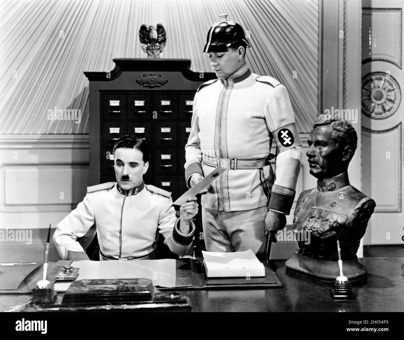 Charlie Chaplin, humoriste qui a prouvé que les actes sont plus forts que les mots avec sa pantomine divisée, va bientôt publier son nouveau tableau, « le Grand dictateur », dans lequel il fait une gifle retentissante sur les régimes totalitaires. Quand le miroir est tenu devant les conquérants frognants de l'autre côté de la mer, ils s'effondrent en figures ludicrose et font le porte-bec secouer avec la fille. Voici le « Grand dictateur ». Il est assis à un bureau, inquiet peut-être de sa mauvaise planification économique. 16 août 1940. (Photo d'ACME). Banque D'Images