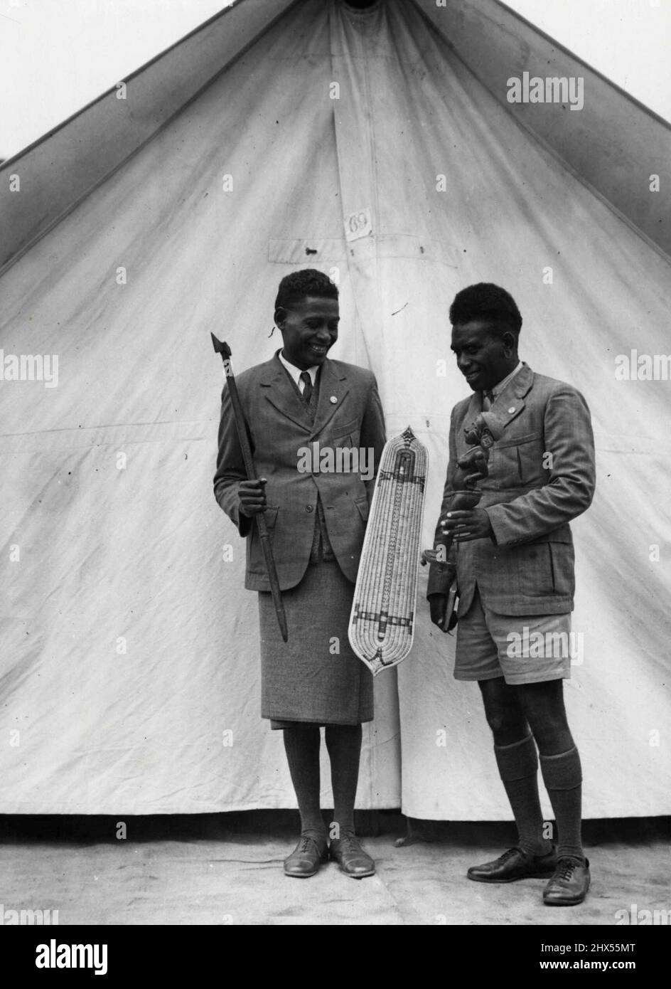 Ils ont hésité dans la frise froide de Melbourne, mais la pluie ne pouvait pas étouffer leurs esprits, William Otimaekera (à droite) et Rovert Salau, des îles Salomon, ont souri joyeusement alors qu'ils ont exposé leurs îles curieuses aujourd'hui. Ils sont ici pour assister au camp adventiste du septième jour au parc royal. 23 janvier 1939. Banque D'Images