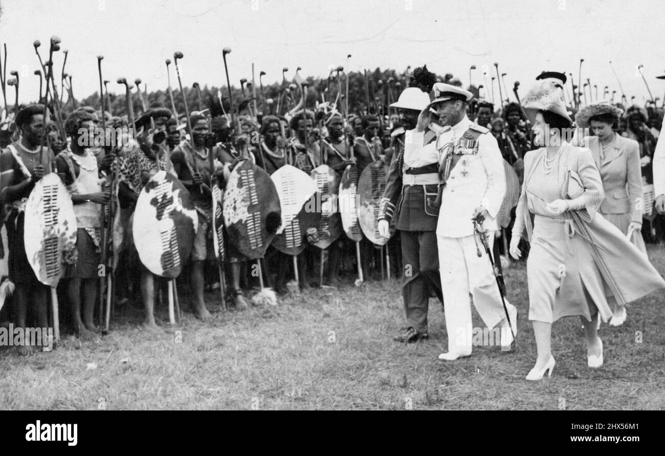 Leurs Majestés inspectés ***** Guerriers -- le Roi salue comme leurs Majestés, accompagné du chef du Paramount Sobhuza Dlamini II, inspecta certains des 4 000 guerriers swazis qui se sont rassemblés le 25 mars. Le chef du Paramount a été élevé dans la hauteur de la mode militaire du deuxième empire, dans une tunique d'azur, un pantalon de écarlate, des pattes d'or et une ceinture diagonale jaune. Au cours de sa tournée en Afrique du Sud, le défunt roi a rencontré ces guerriers swazis en tenue de guerre complète. Le défunt roi est accompagné de la reine Elizabeth et de la nouvelle reine. 23 juillet 1947. Banque D'Images