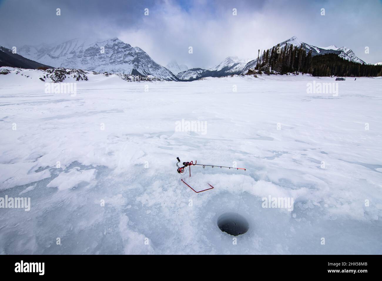 Canne de pêche sur glace et trou de tarière sur le lac gelé Kananaskis avec les montagnes Rocheuses canadiennes en arrière-plan en Alberta Canada Banque D'Images