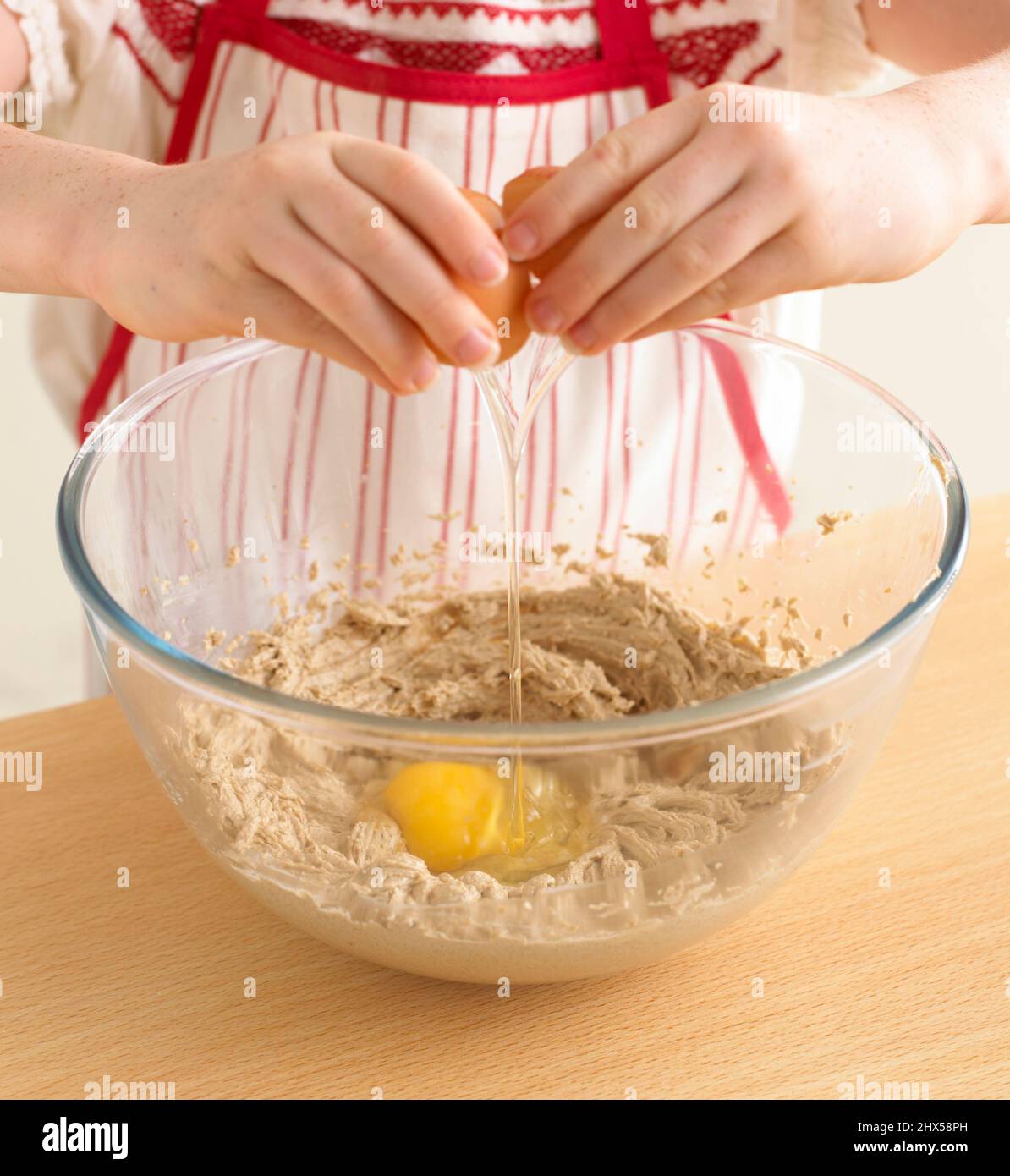 Petite fille cassant l'œuf sur les ingrédients de la pâte au chocolat dans un grand bol à mélanger, gros plan Banque D'Images