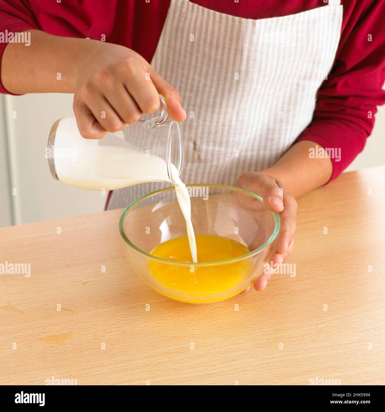 Garçon versant du lait du pot sur le plateau à œufs dans un bol en verre, gros plan Banque D'Images