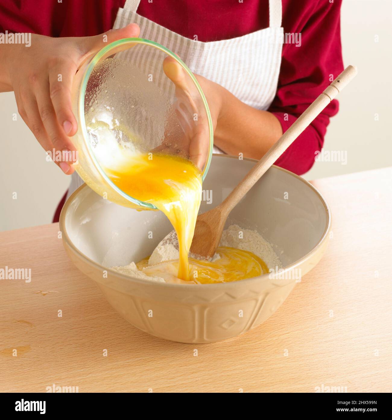 Garçon versant un œuf de la cuvette de verre dans un grand bol contenant une cuillère en bois, gros plan Banque D'Images