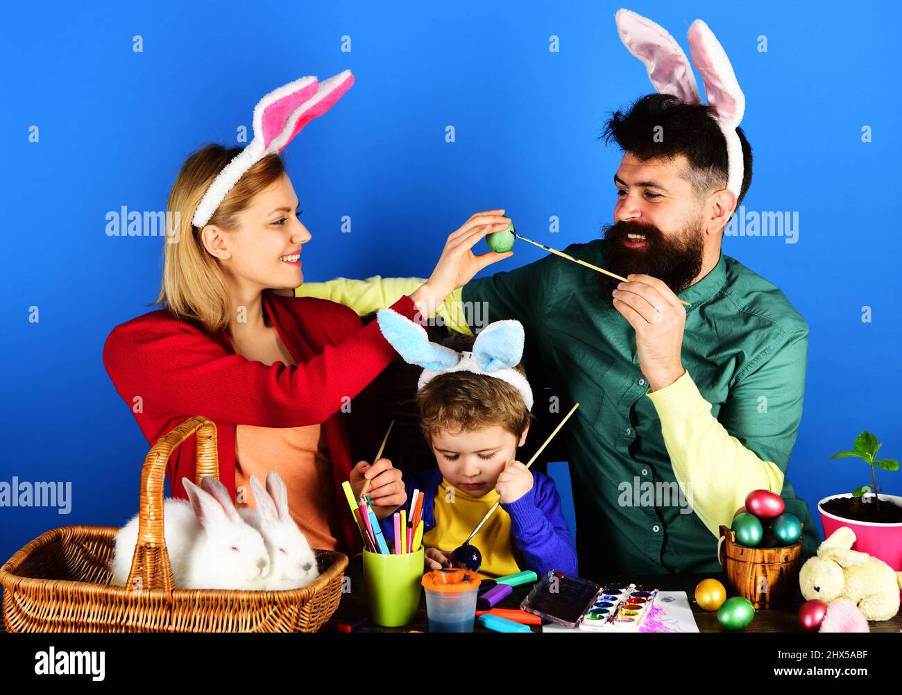 Famille de lapins le jour de Pâques. Mère, père et fils peignant des œufs. Bonne famille dans les oreilles de lapin. Banque D'Images