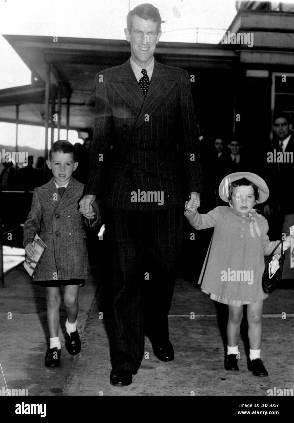 Sir Edmund Hillary, qui a quitté le bateau-mouche de la baie rose ce matin par Teal Airways, descend le Gangway à bord de l'avion avec deux des plus jeunes passagers à Auckland, en Nouvelle-Zélande. Ross Gilmore cinq ans et Yvonne Gilmore trois ans. Les deux enfants sont en route pour voir leur grand-mère qui vit dans la rue à côté de l'endroit où vit Sir Edmund Hillary. Les parents des enfants de Gilmore se joignent à leurs enfants plus tard pour se mettre en résidence en Nouvelle-Zélande après avoir vécu en Nouvelle-Guinée. 12 août 1953. Banque D'Images
