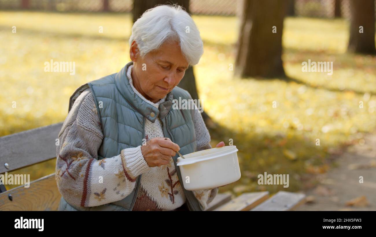 Une femme caucasienne âgée, sans abri, est assise sur un banc à l'extérieur et mange de la soupe chaude qui lui a été donnée par un groupe de bénévoles. Photo de haute qualité Banque D'Images