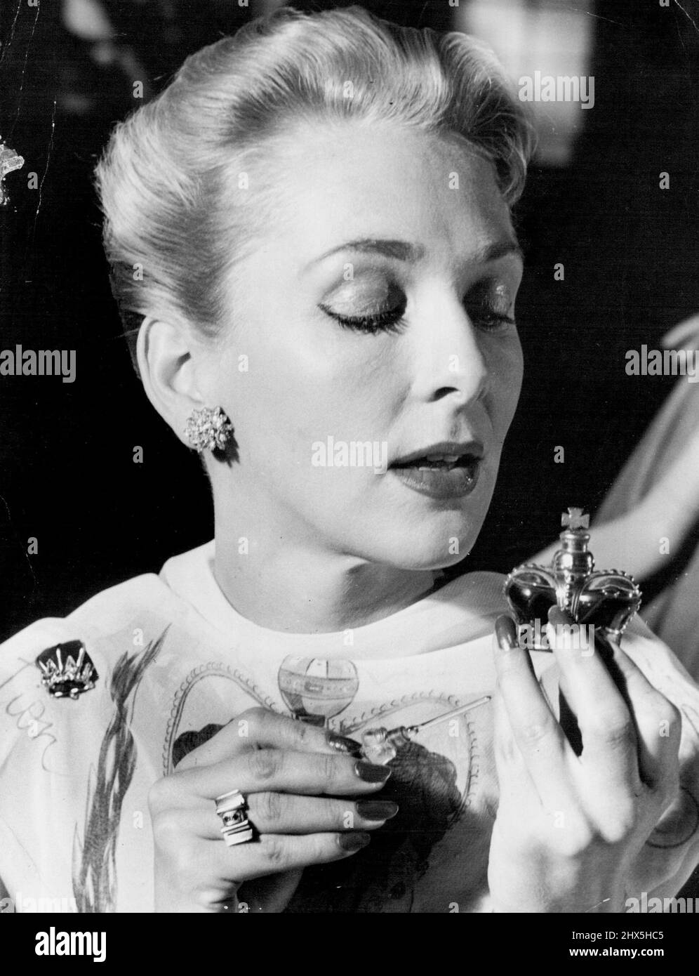 Portant un foulard de couronnement peint à la main Dorothy McCullogh essaie un peu de parfum de couronnement vendu dans une bouteille en forme de couronne de bijoux pour £16. Elle épingle le foulard à son épaule avec un petit modèle de velours de la couronne. 4 juin 1953. Banque D'Images