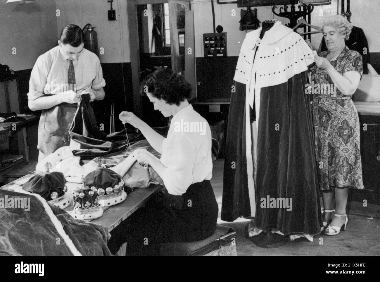 Préparation pour le couronnement travailler sur le collier d'une robe de Viscount est Mary McGetting (caméra la plus proche) pendant Reg Jackson rade le jambon. Mme Cross (à droite) fait les derniers points à une robe Barons. Les tailleurs et les tailleurs de l'un des plus grands pourvoyeurs de location de Londres sont maintenant occupés à s'assurer que les robes et couronnement de couronnement qui seront loués et portés par Barons et Viscomtes sont en bon état. Les robes, qui coûtent aujourd'hui environ £500 - mais elles peuvent être louées des grandes entreprises d'équipement pour £25 complet avec Coronet. 26 août 1952. (Photo de Sport & General Press Agency, Banque D'Images Préparation pour le couronnement travailler sur le collier d'une robe de Viscount est Mary McGetting (caméra la plus proche) pendant Reg Jackson rade le jambon. Mme Cross (à droite) fait les derniers points à une robe Barons. Les tailleurs et les tailleurs de l'un des plus grands pourvoyeurs de location de Londres sont maintenant occupés à s'assurer que les robes et couronnement de couronnement qui seront loués et portés par Barons et Viscomtes sont en bon état. Les robes, qui coûtent aujourd'hui environ £500 - mais elles peuvent être louées des grandes entreprises d'équipement pour £25 complet avec Coronet. 26 août 1952. (Photo de Sport & General Press Agency, Banque D'Images