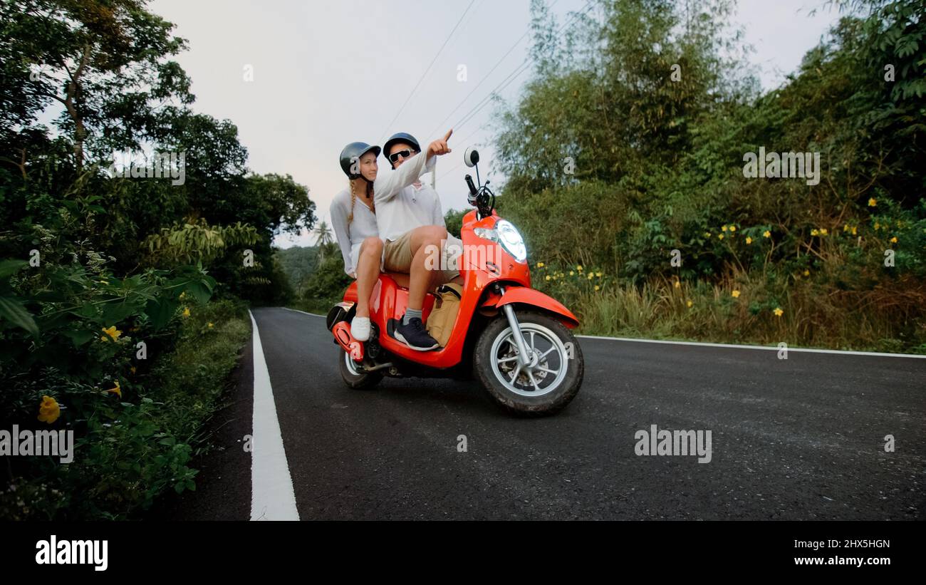 Trajet en scooter. J'adore un couple sur une moto rouge vêque de vêtements  blancs sur la route forestière. Juste marié femme et homme baiser, les  hugs, s'asseoir sur la moto. Mariage, lune