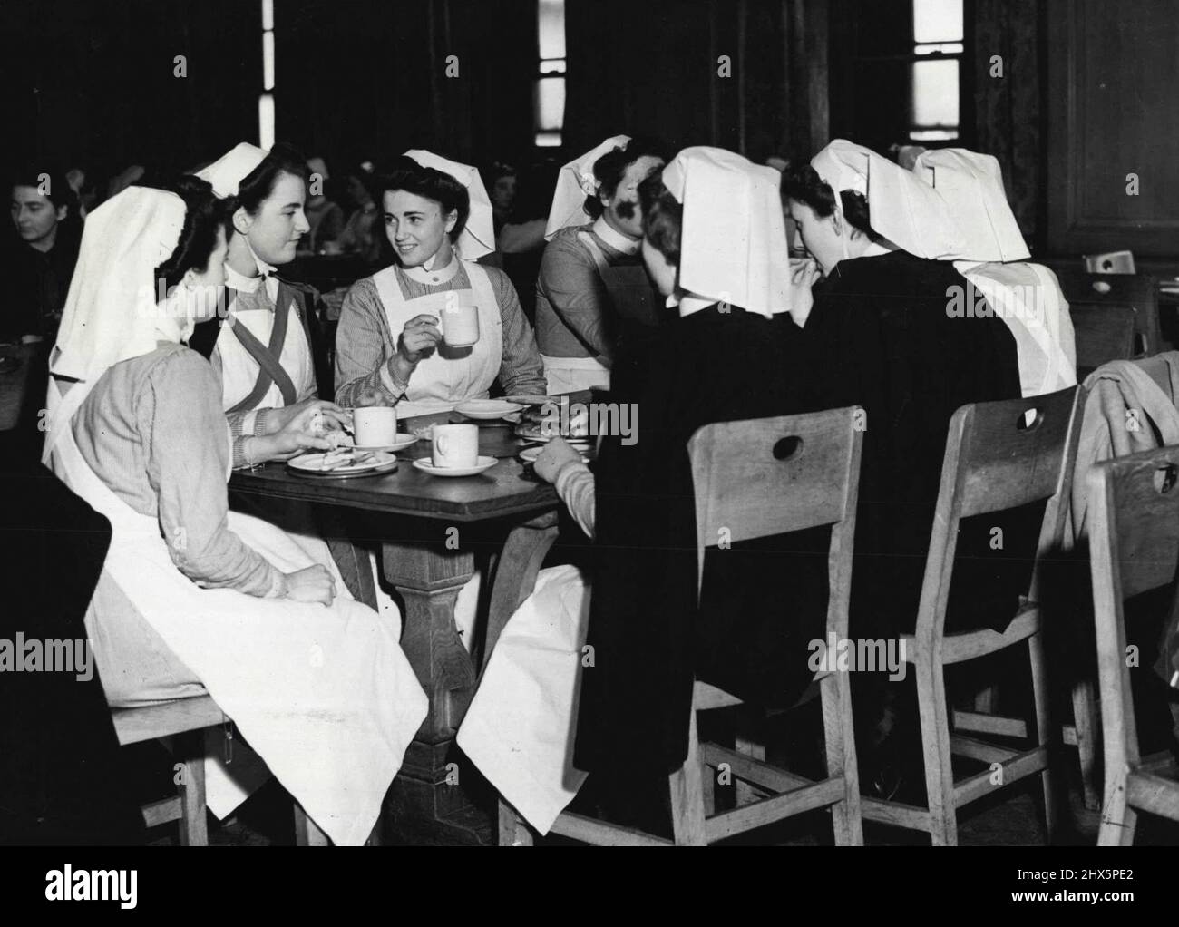 Tea Time -- les infirmières ont le petit déjeuner à 6,30 h,; dîner chaud (deux plats avec un choix de plats) à 12 h; thé à 4,30 h et un souper chaud (encore deux plats) à 9 h - Nurse Phillips (troisième de gauche) prend maintenant le thé avant de retourner en service et a changé en uniforme. - Les thés varient tous les jours, - cet après-midi, les infirmières ont des petits pains. - La salle à manger dans les infirmières. La maison peut accueillir 160; le mobilier est plus attrayant étant le chêne non coloré; tapis verts contraste agréablement quand les tables sont posées. Des fenêtres à deux fenêtres s'ouvrent sur le court de tennis. 18 septembre 1943. Banque D'Images