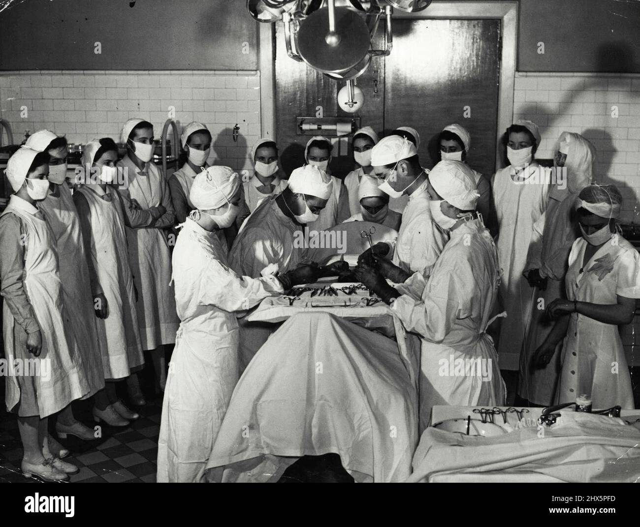 Woman in White -- une opération en cours alors qu'une classe d'infirmières de la première année regarde dessus. Cette formation à 'le ringside' est nécessaire pour durcir leurs nerfs à la procédure, car il ne doit pas y avoir de grincement, d'incertitude ou de nervosité, quand ils aident à l'opération. La vue du sang ne doit pas non plus causer de vaciller dans leur travail. 12 avril 1942. (Photo par International News photos). Banque D'Images