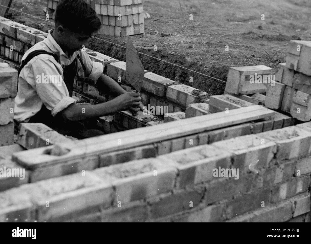 Le garçon Saunders de Ealing. L'apprenti le plus jeune au travail est Kiwi Keith Atkinson, âgé de 14 ans, qui apprend à être un brickmayer. Même l'apprenti garçon d'Ealing, âgé de 14 à 17 ans, a terminé avec succès la construction de quatre maisons sur le domaine du Conseil d'Ealing à Townholm Crescent Hanwell, et a maintenant été donné la tâche de construire deux autres. Travaillant sous la direction de contremaîtres et d'instructeurs d'un entrepreneur local, les garçons sont de plus en plus compétents et sont ravis de leur su Banque D'Images
