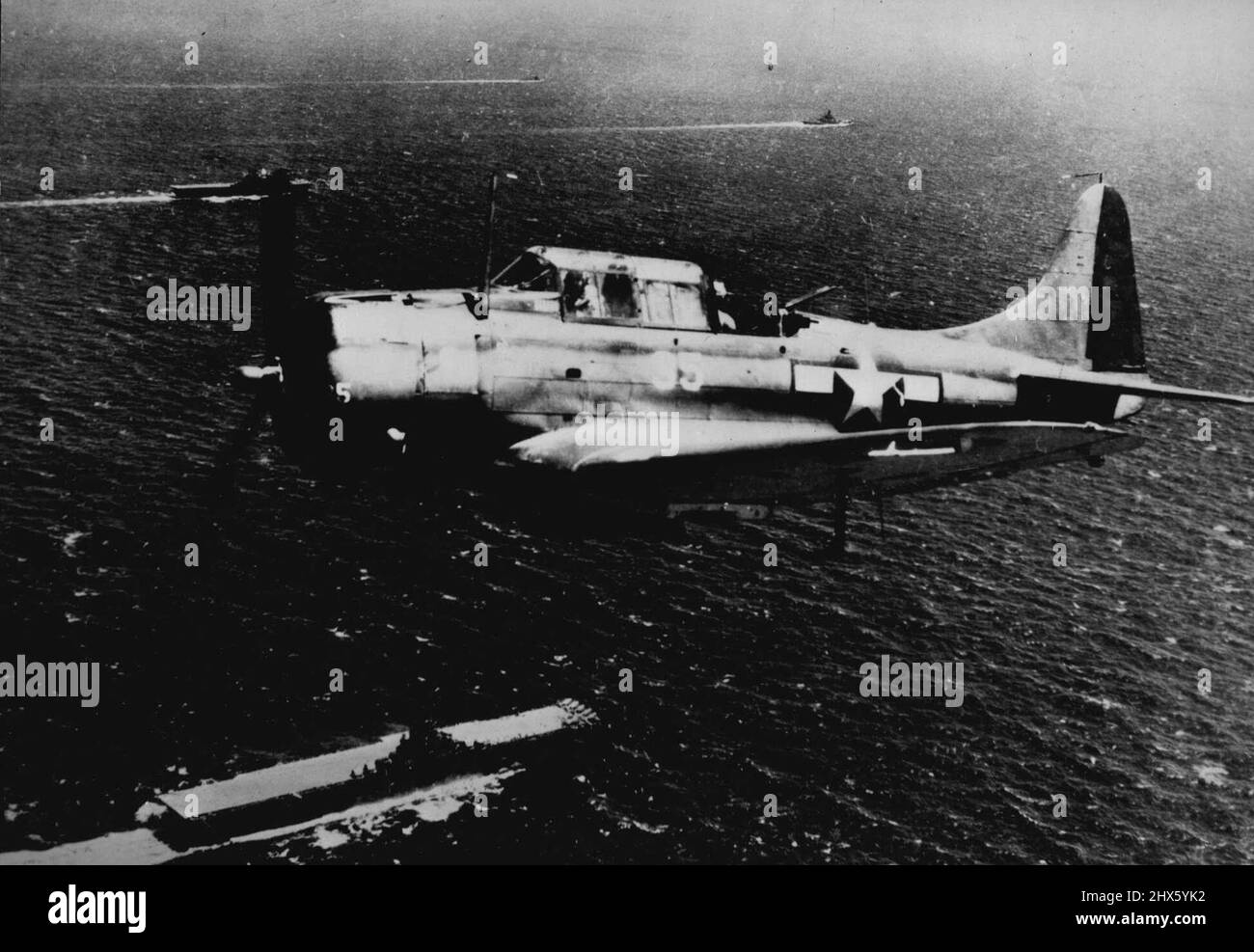 Les chefs de la Force opérationnelle des transporteurs de la Marine américaine pour la grande base japonaise -- Une bombe a claqué sous son fuselage, un bombardier-plongée de la Marine américaine survole les unités d'une force opérationnelle de la Marine américaine qui traverse le Pacifique central vers Palau, base japonaise stratégique dans les îles Caroline. Deux porte-avions (en bas à gauche et en haut (à gauche) et un cuirassé (en haut à droite) sont visibles, tandis que les éprises blanches marquent d'autres unités de la force. Lors d'une récente attaque aérienne et maritime de trois jours sur les places fortes ennemies dans les carolines de l'Ouest, Banque D'Images