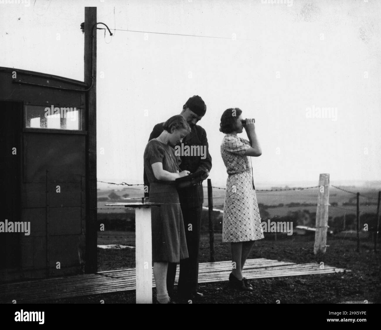 Department of Air -- les femmes observatrices jouent un rôle important dans le corps australien d'observateurs de l'air volontaire en pleine expansion, dont les membres fournissent une montre 24 heures sur 24 pour les avions qui passent par-dessus leurs secteurs. Le corps est l'un des services les plus essentiels liés à la R.A.F., et la Force aérienne maintient une liaison étroite avec ses membres. Ici, un officier de R.A.A.F. vérifie le travail d'un quart de travail féminin, ou « tour », en service à un poste d'observateur quelque part à Victoria. Les journaux non victoriens substit Banque D'Images