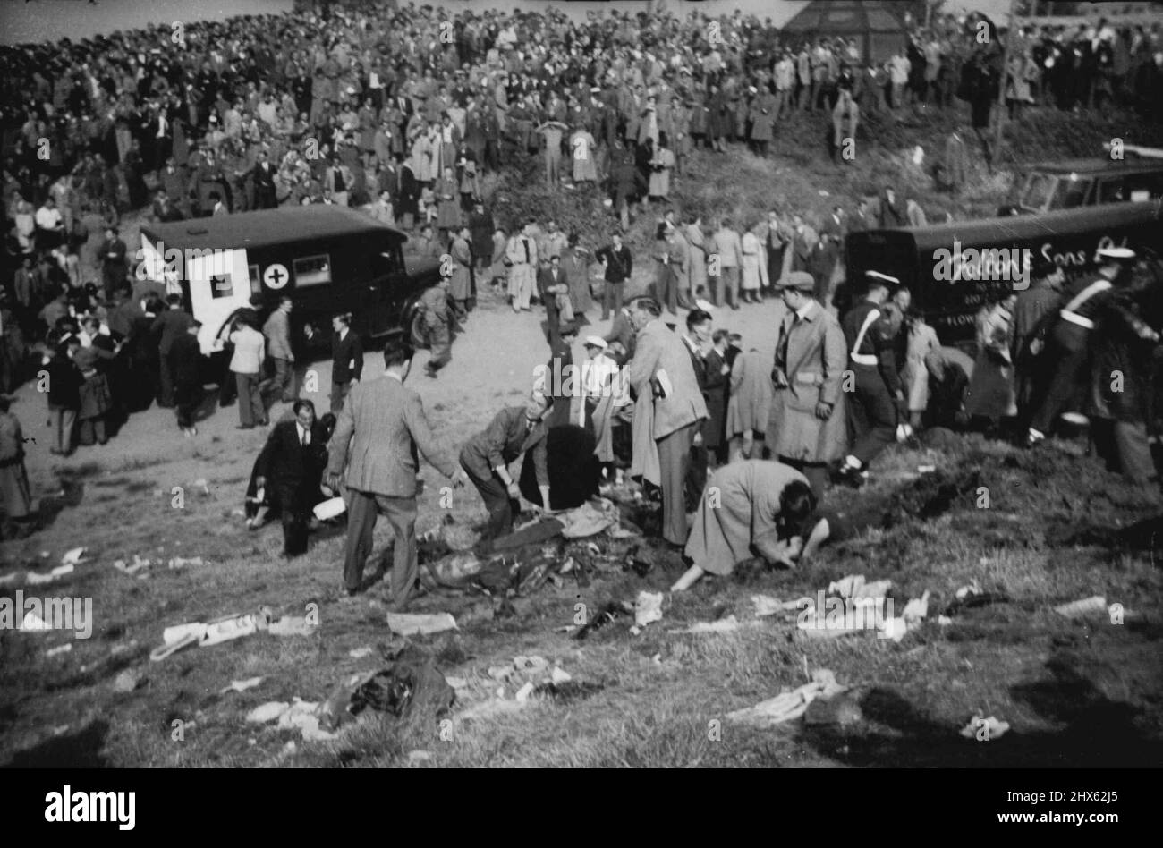 Lorsque la mort des airs a frappé le Farnborough Hillside, la sombre scène sur le flanc de la colline où les spectateurs ont été tués et blessés des blessés sont sur le sol comme premier et est donné. En arrière-plan, il y a une ambulance et une foule qui se mêle de manière stupéfaite et étourdi. Vingt personnes - le pilote John Derry et un passager et 18 spectateurs ont été tués et 35 spectateurs ont été blessés lorsque le prototype no 1 du semi-secret de Havilland 110 a explosé à l'air de Farnborough (Hampshire) Banque D'Images