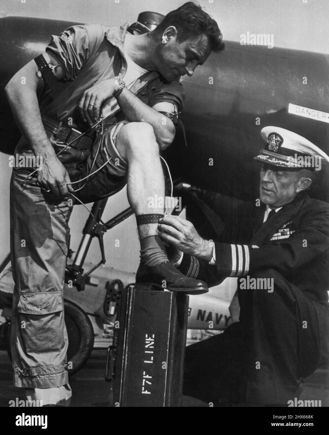 Câblé pour Sound Jet Flying -- chirurgien de vol de la marine Comdr. Norman L. Barr attache des électodes au corps du chef de pilote Joseph Kube lors de la série de tests et d'expériences réussis de la Marine pour vérifier les esprits et les corps des pilotes d'avions à réaction en vol. Les électrodes enregistrent, par le biais d'appareils radio complexes, les réactions cardiaques et respiratoires au cours des différentes étapes du vol. L'équipement a été mis au point en raison du nombre de catastrophes aériennes causées par une « défaillance pilote ». Novembre Banque D'Images