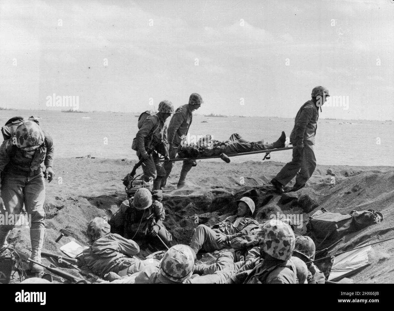 Blessé Marine obtient de l'aide sur Iwo Beach -- les Corpmen portent un blessé Marine vers un bateau d'évacuation sur la plage à Iwo Jima tandis que d'autres marins se caucus dans Foxholes. 25 février 1945. (Photo de Joe Rosenthal, Associated Press photo). Banque D'Images