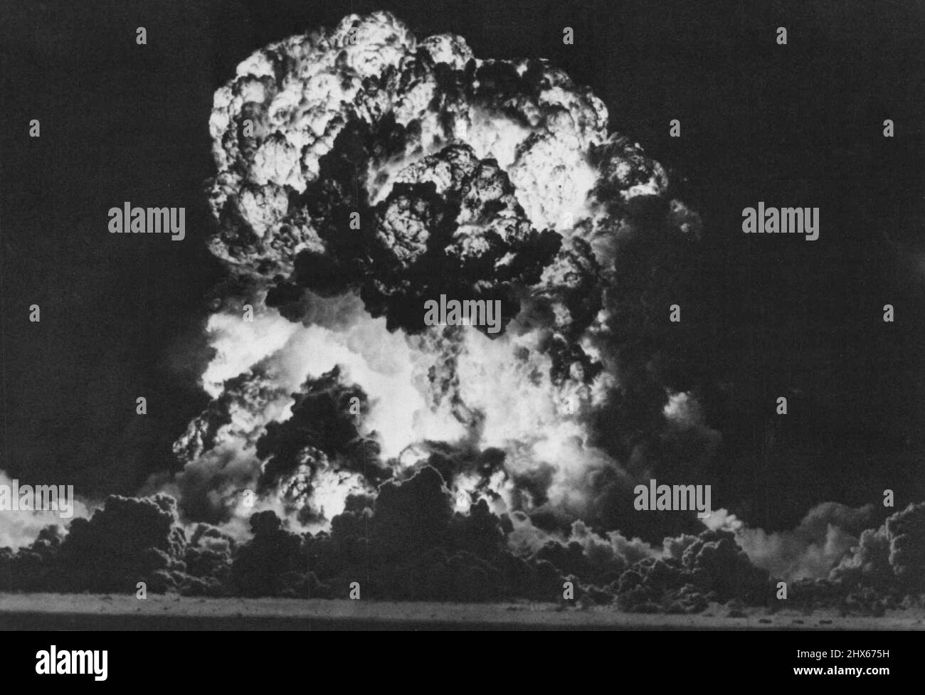 Site d'essai atomique -- la boule de feu atomique de 'opération Cue'  s'étend sur le fond du désert et s'étend vers Survival Town. Trois des  maisons utilisées dans le test FCDA peuvent