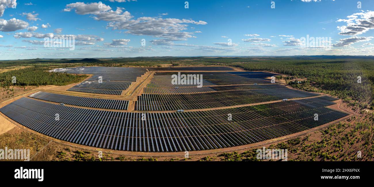 Vue aérienne d'une vaste ferme solaire avec des rangées de panneaux photovoltaïques au milieu d'un paysage boisé sous le ciel bleu Banque D'Images