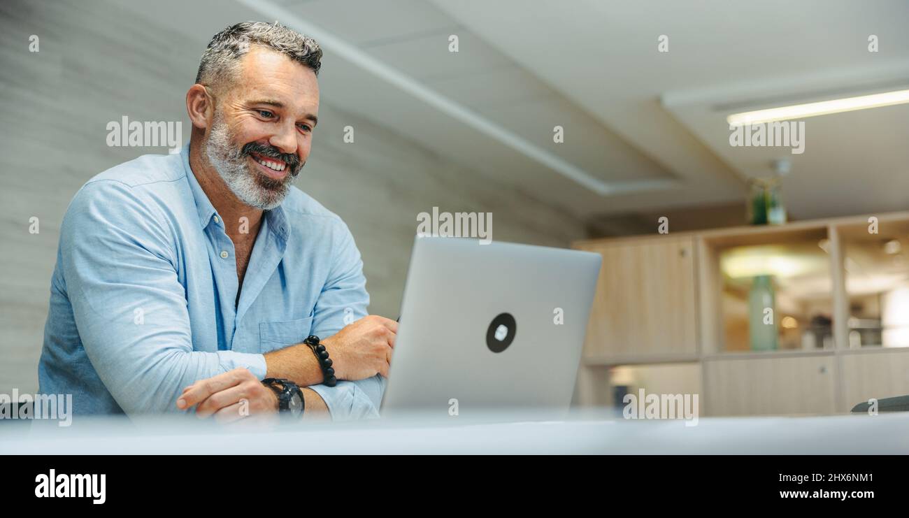 Entrepreneur joyeux assistant à une réunion en ligne avec ses associés d'affaires. Homme d'affaires heureux et mature ayant une visioconférence tout en travaillant à distance Banque D'Images