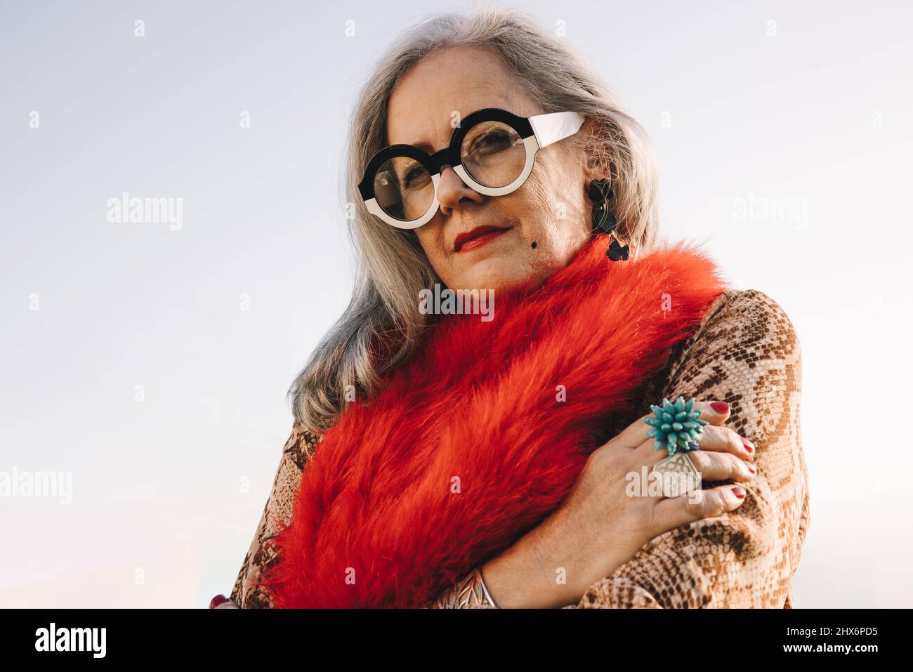 Femme aux cheveux gris regardant l'appareil photo en plein air. Femme âgée élégante portant des vêtements décontractés colorés et des lunettes. Femme âgée Banque D'Images