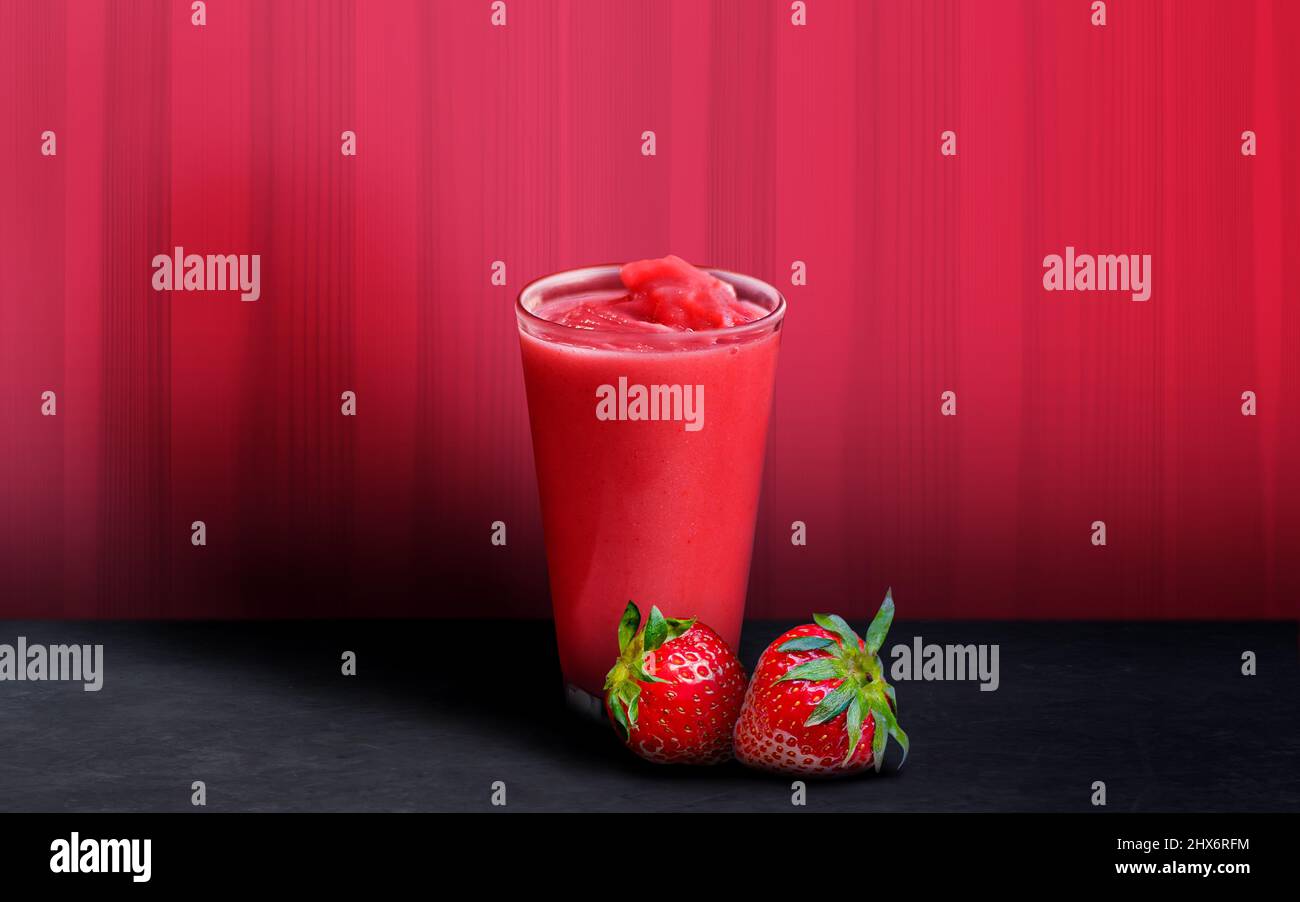 jus de fraise dans un verre avec deux fruits de fraise sur fond rouge Banque D'Images