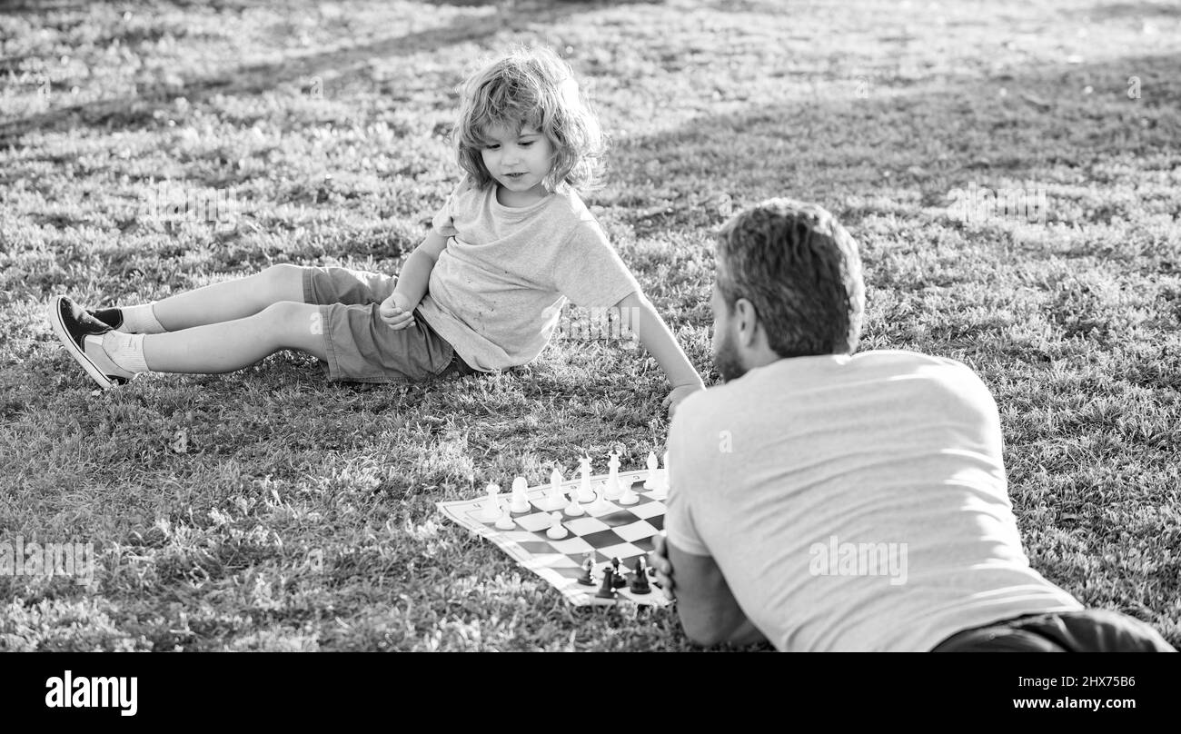 bonne famille de papa et garçon de fils jouant aux échecs sur l'herbe verte dans le parc extérieur, parent Banque D'Images