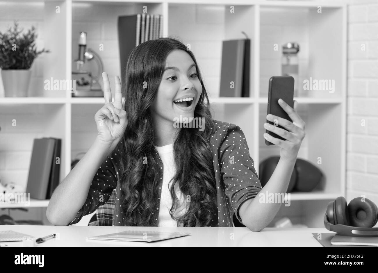 des cheveux longs et bouclés étonnés pour les enfants prenant une photo de selfie sur un smartphone montrant un geste de paix, un blogging Banque D'Images