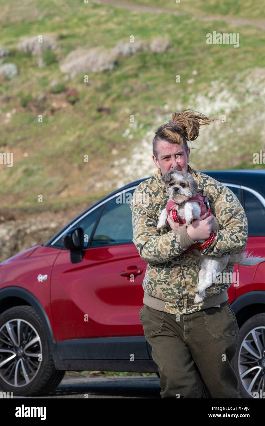 Un propriétaire de chien portant un petit chien dans un vent fort. Banque D'Images