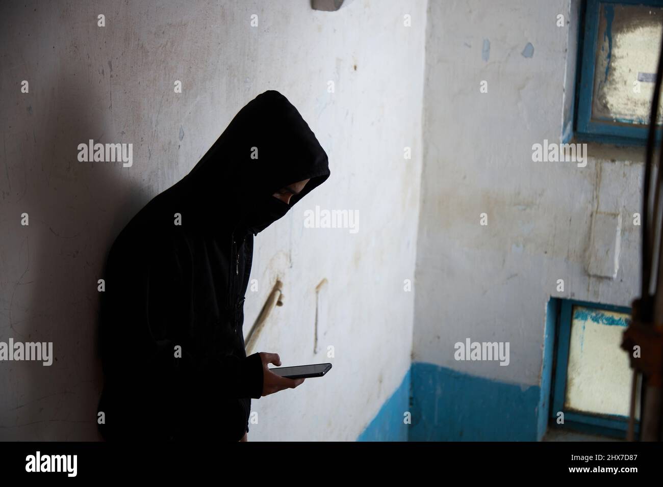 un maniaque, un voleur, un homme dans une cagoule noire est debout sur les escaliers, en utilisant le téléphone. Banque D'Images