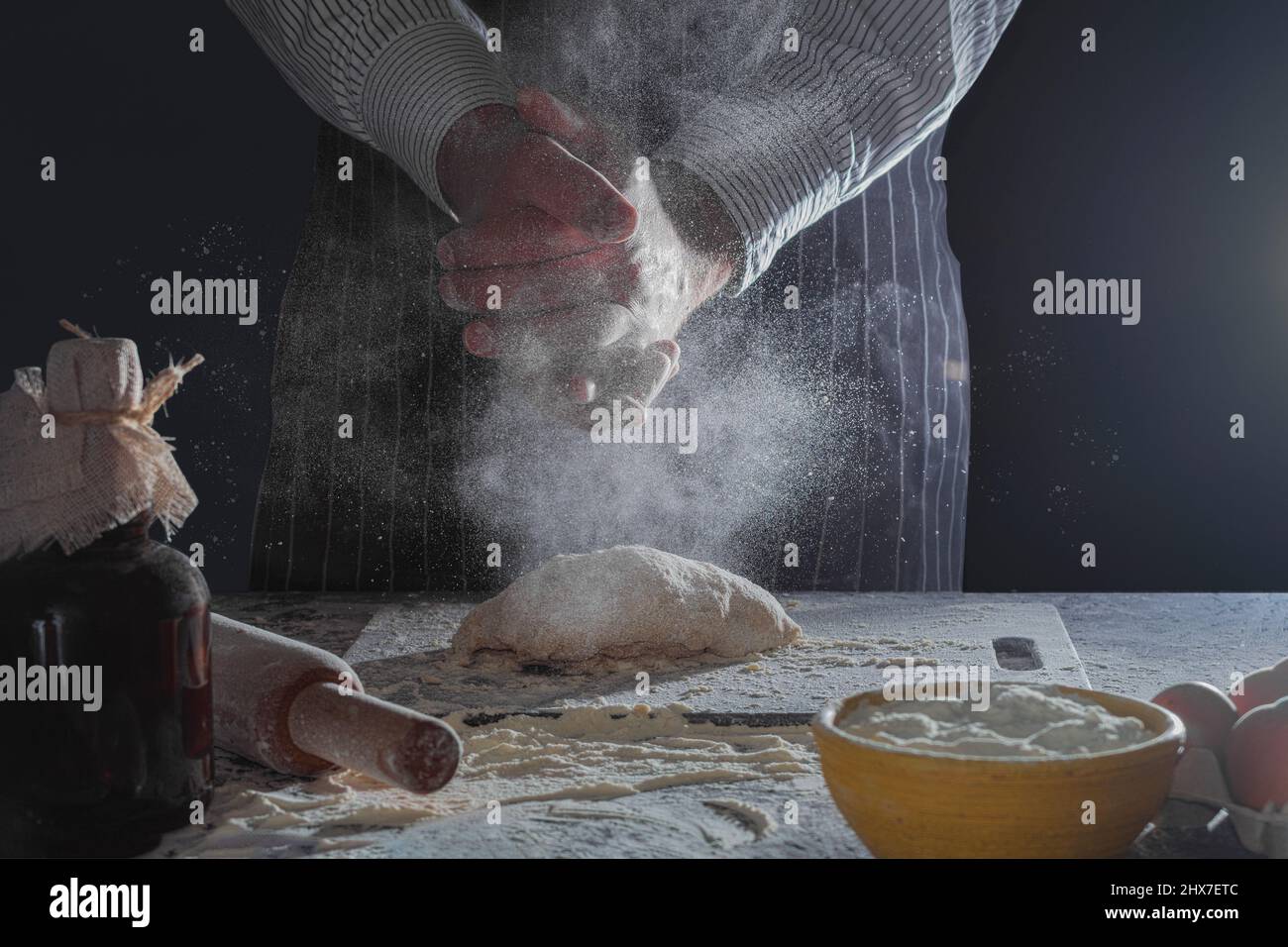 Les mains du cuisinier sont dans la farine et pétrir la pâte. Le cuisinier pétrit la pâte pour la cuisson, fait des éclaboussures de farine. Couleurs décolorées avec foc sélectif Banque D'Images