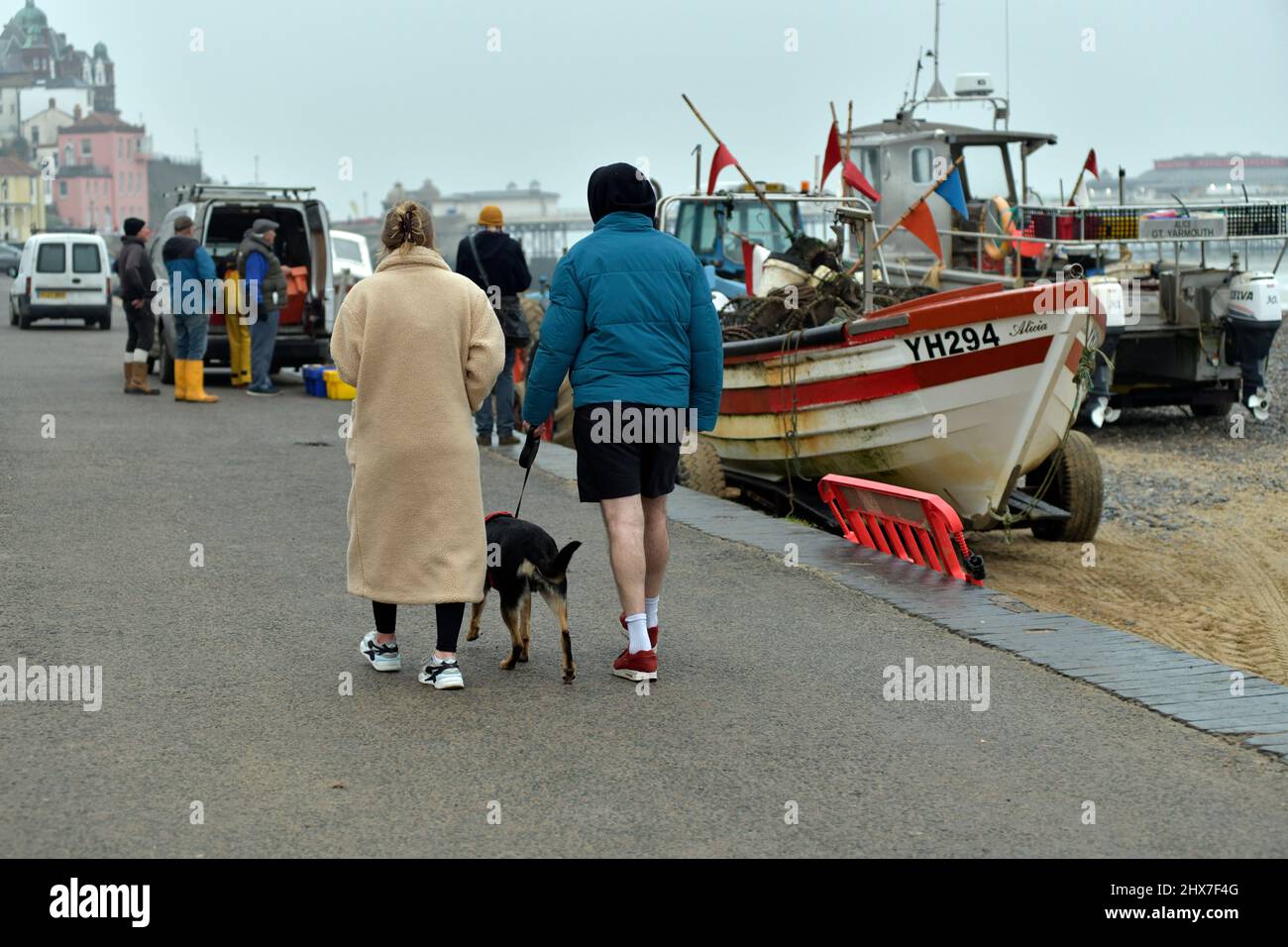 homme et femme marchant chien le long de la promenade près de déchargement pêcheurs cromer norfolk angleterre Banque D'Images