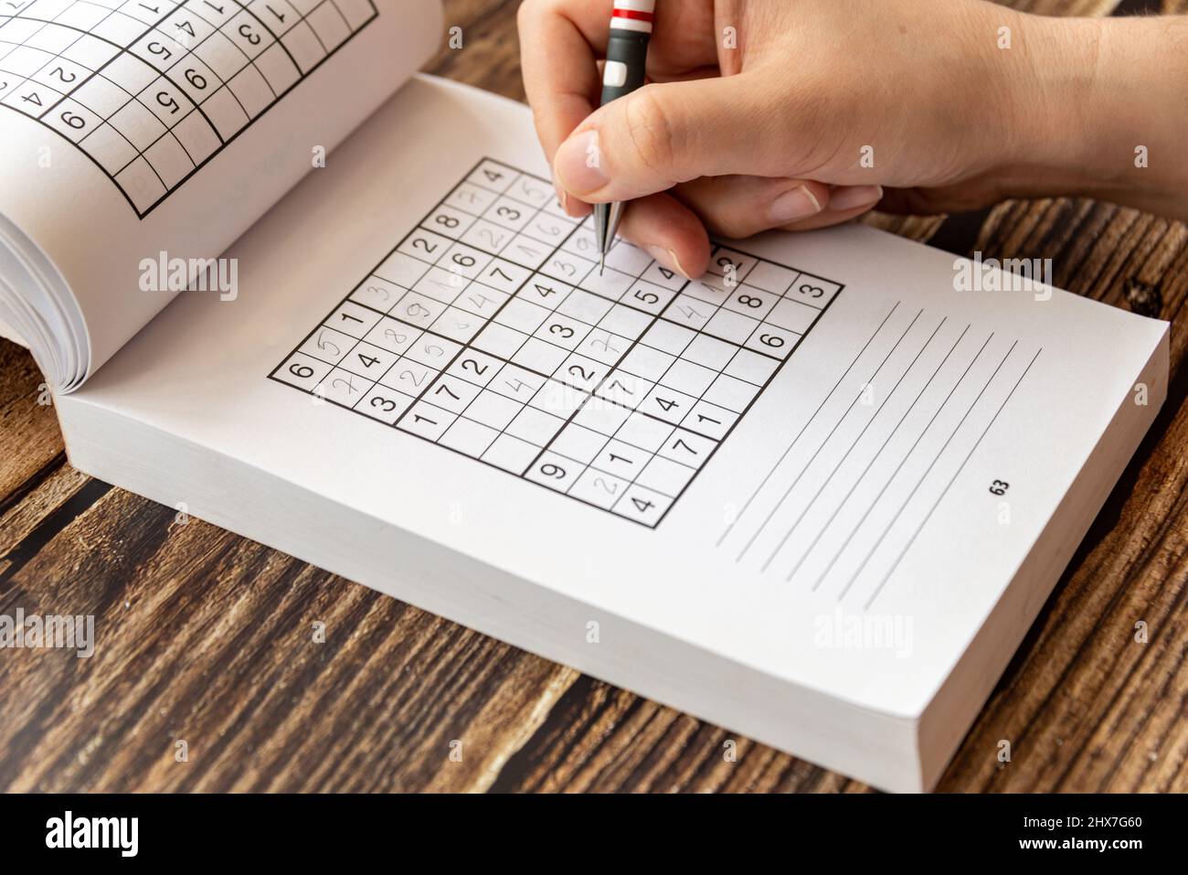 Personne résolvant un puzzle de sudoku sur une table en bois. Banque D'Images