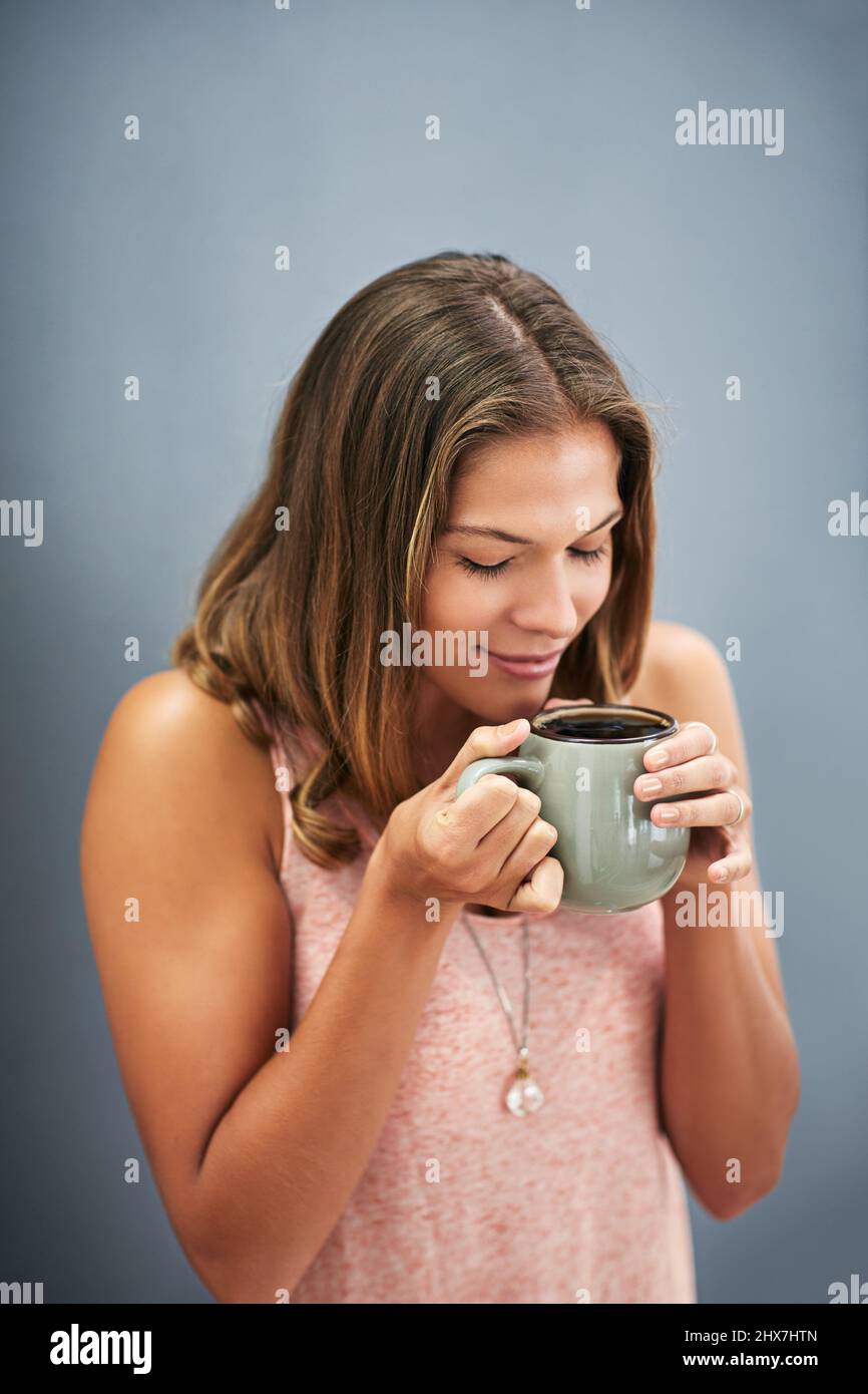 Le café frais sent une odeur incroyable Photo studio d'une jeune femme buvant une tasse de café sur fond gris. Banque D'Images