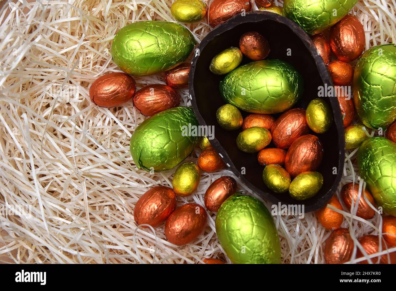 Pile d'œufs de pâques au chocolat enveloppés de papier d'aluminium coloré en vert, orange, jaune et or avec deux moitiés d'un gros œuf de chocolat noir brun. Banque D'Images